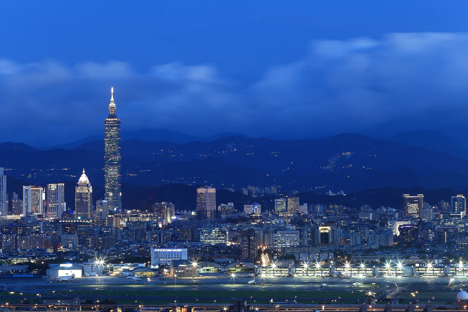 Taipei city skyline at dusk with Taipei 101 rising above clustered towers.